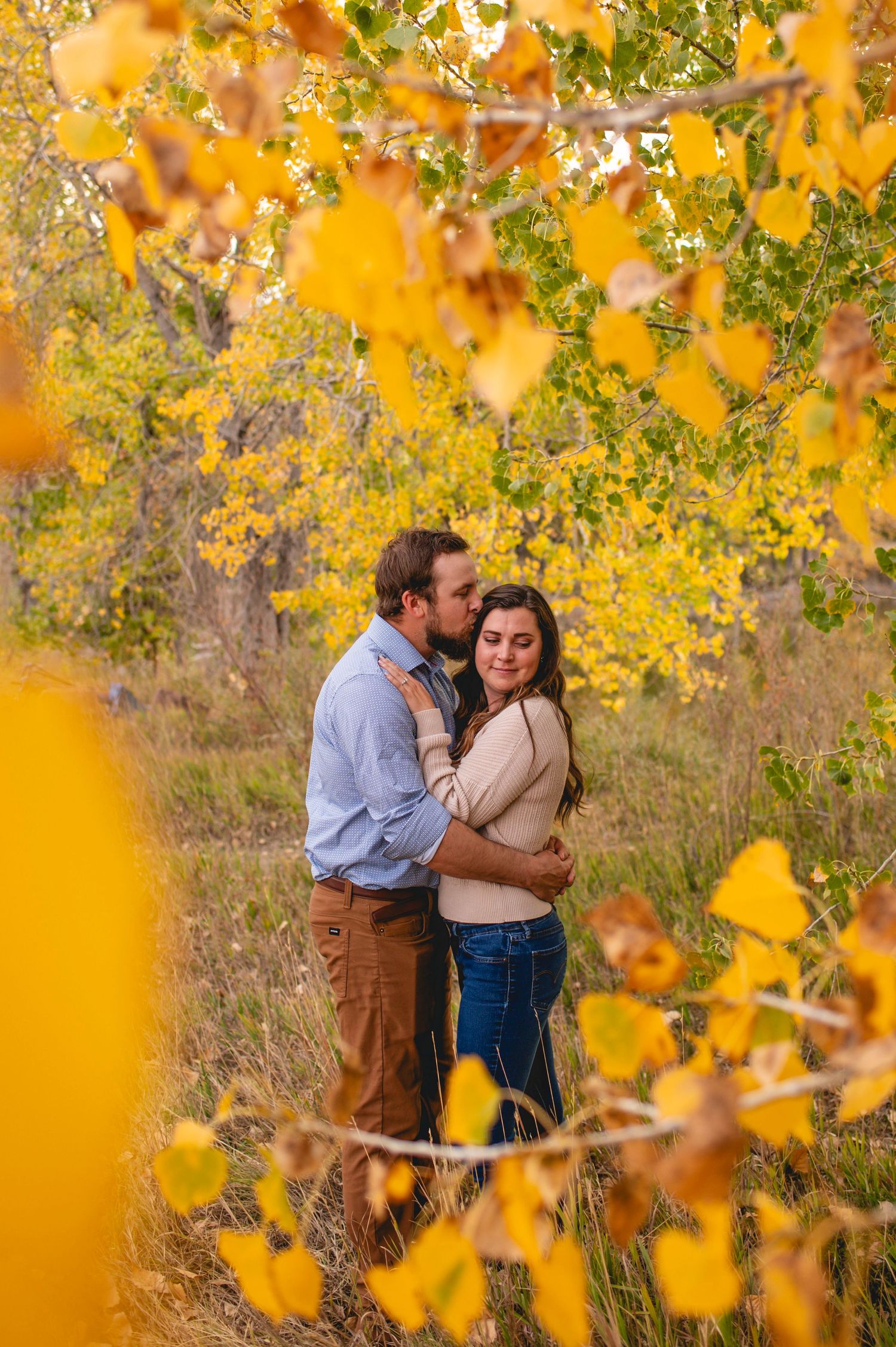Romantic autumn couple embraces among vibrant yellow fall foliage in a natural woodland setting.
