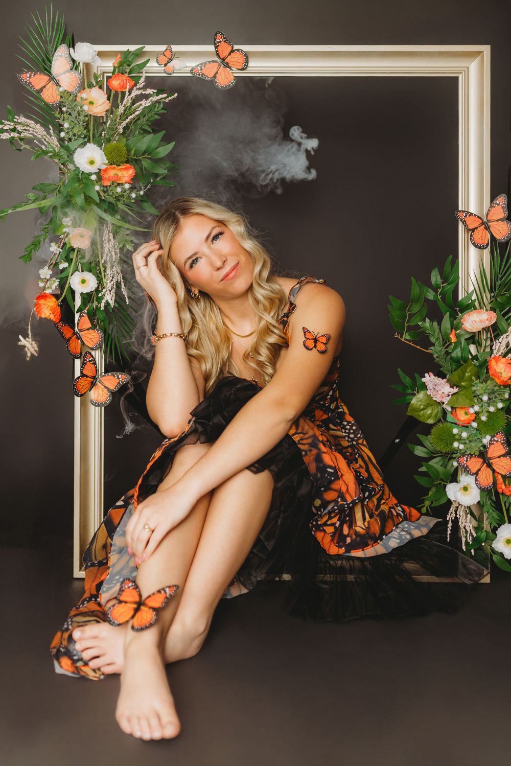 Artistic composition with butterfly dress and floral frame against black background.