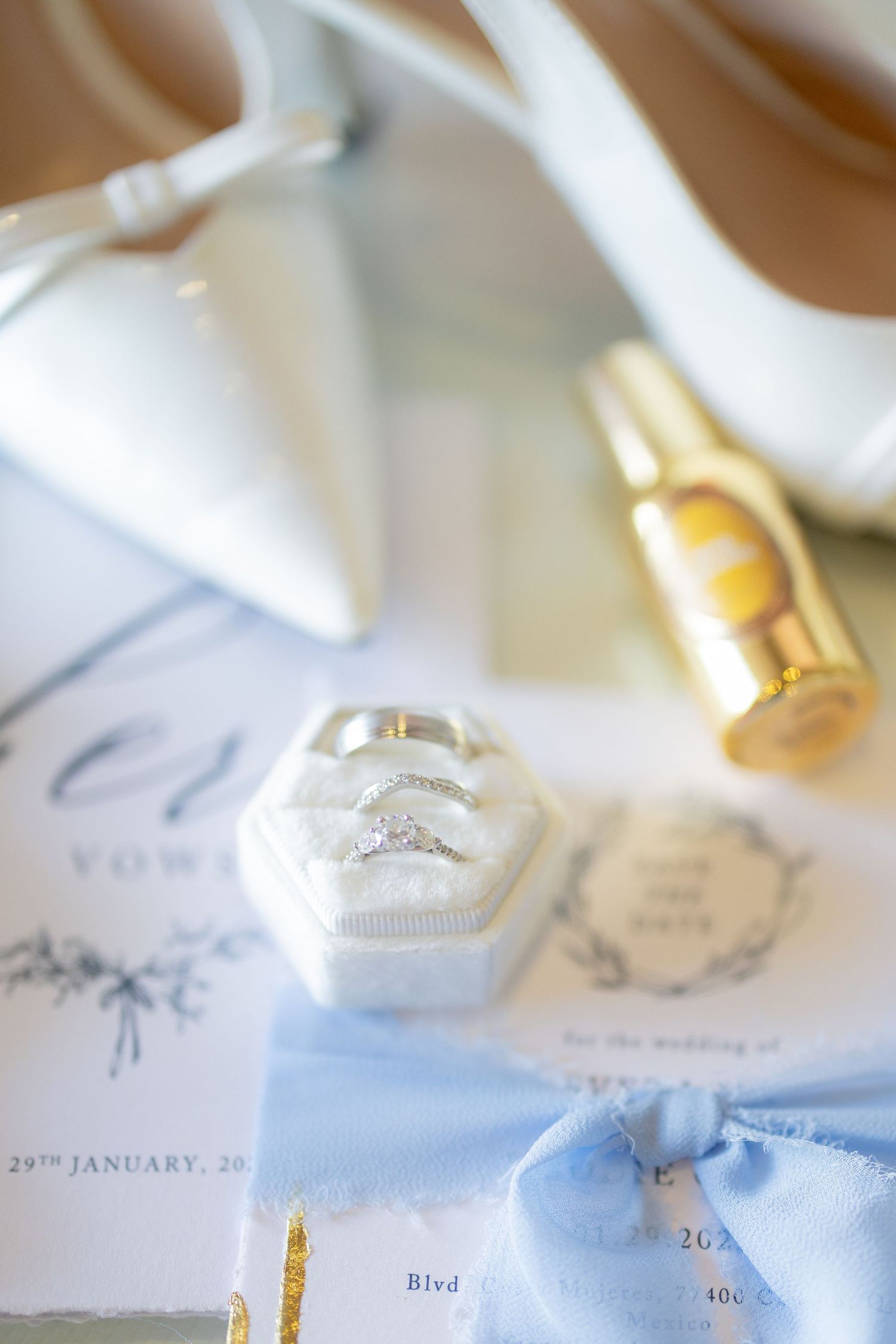 Close-up of wedding rings and invitation details in soft white and gold tones showing elegant wedding day preparations.
