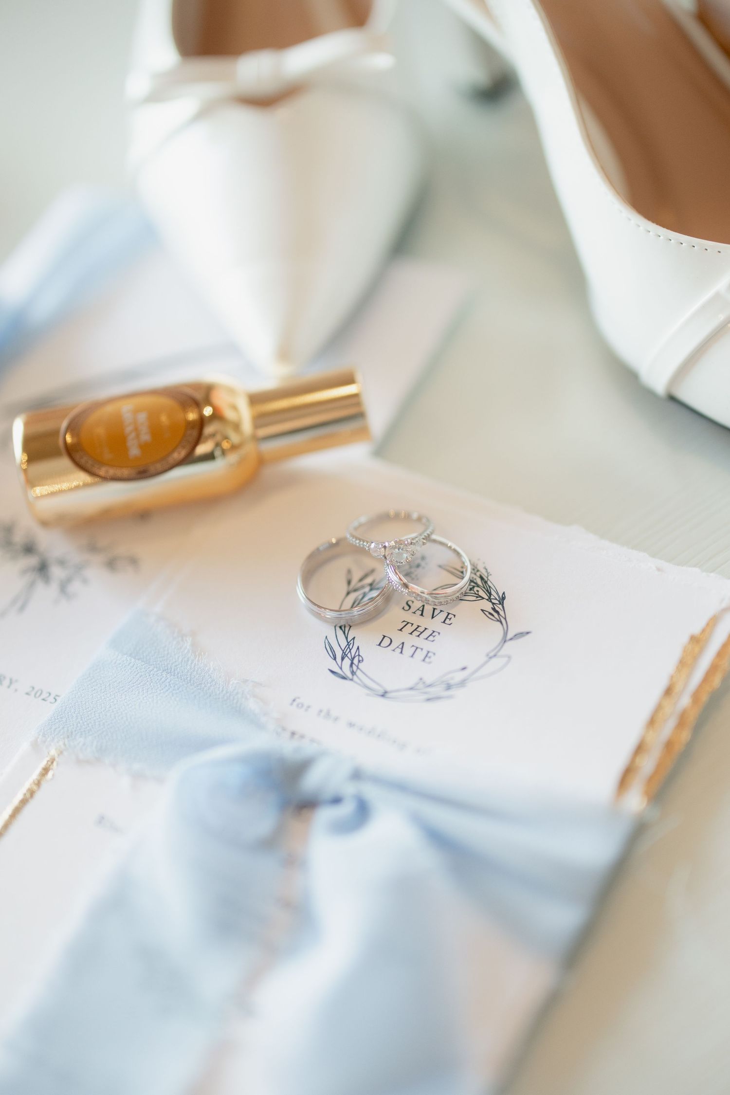 Wedding details including a gold perfume bottle, elegant invitation with light blue bow, and delicate monogram design.