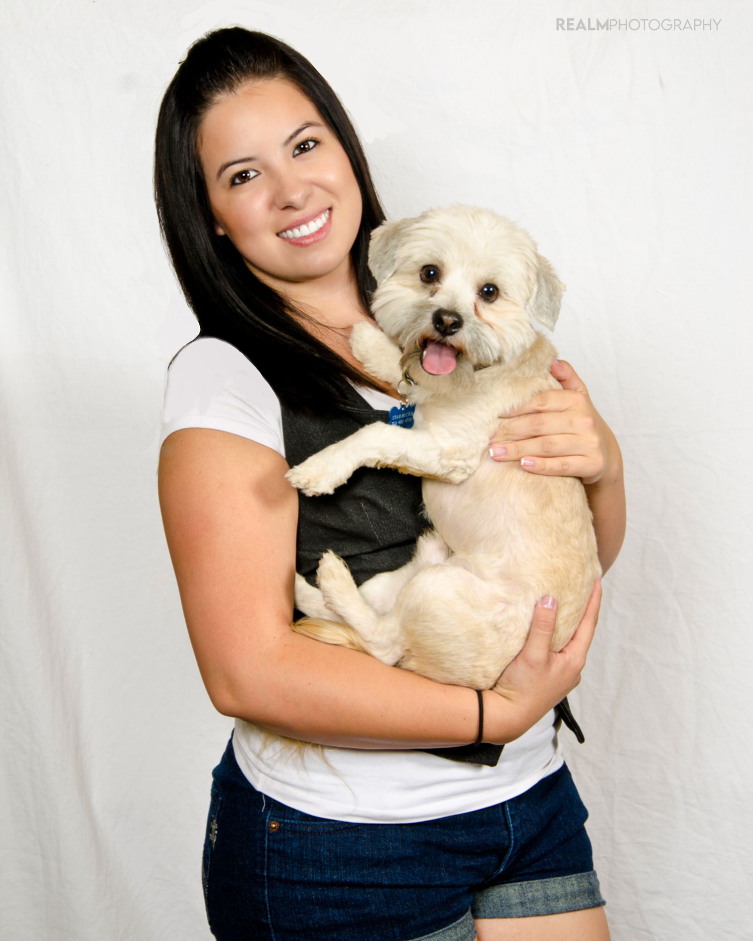 Person embracing a small white fluffy dog against a white studio background.