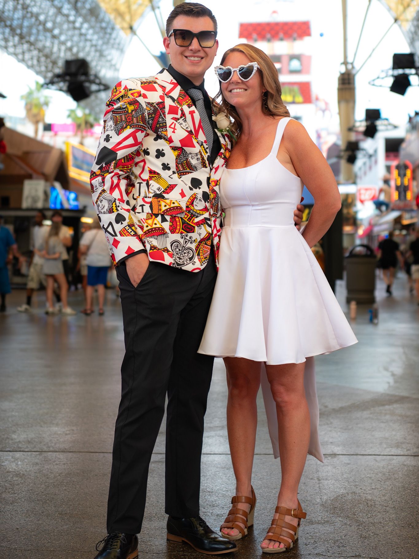 A couple in formal attire, with one in black and one in white, posing together at what appears to be a fair or festival.