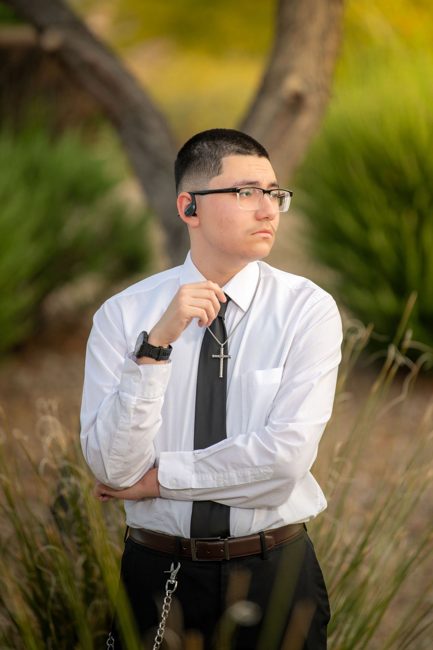 Person in business attire sitting thoughtfully outdoors with natural bokeh background.