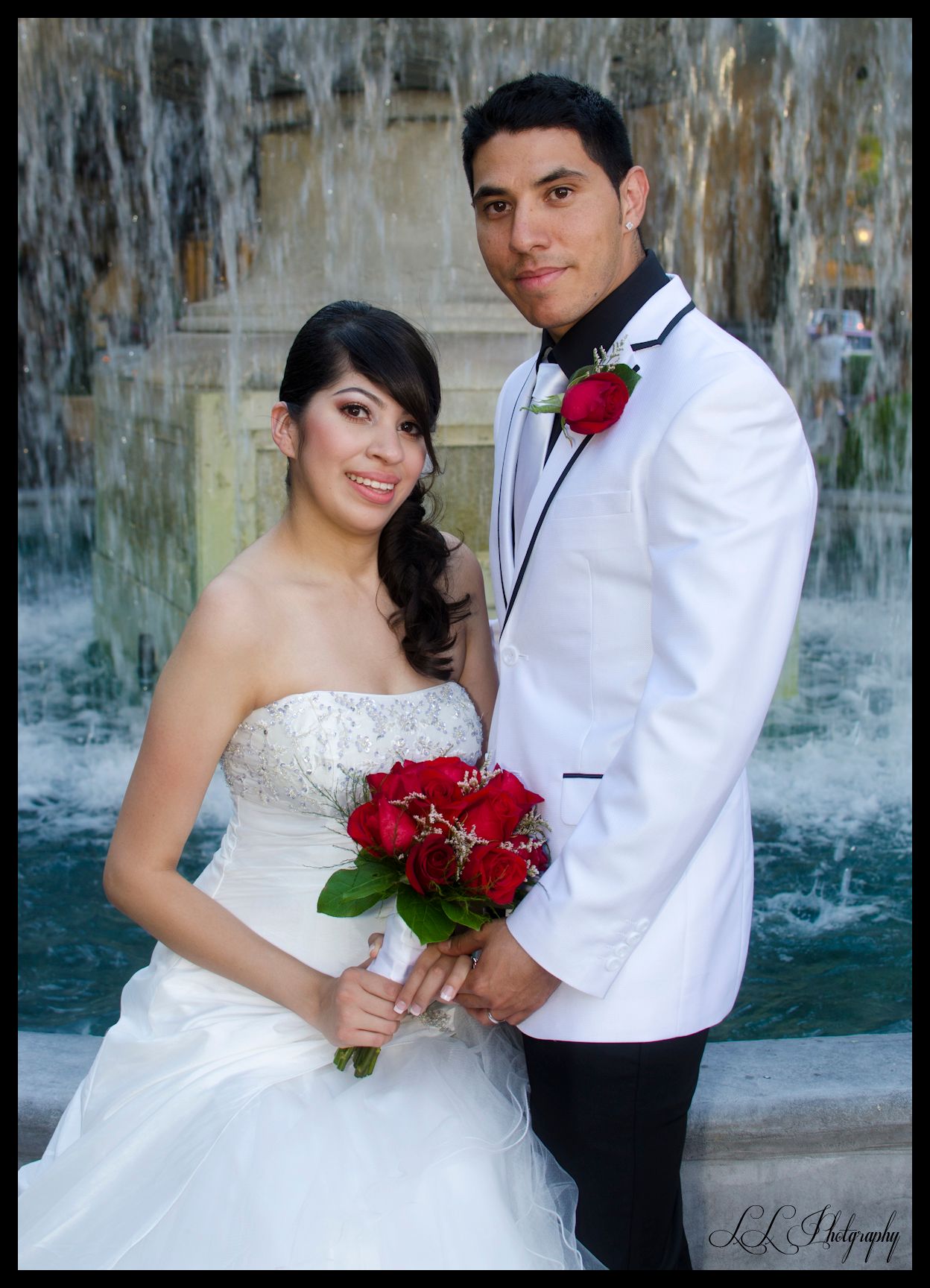 Wedding couple poses by fountain at Las Vegas resort with bride holding red rose bouquet.