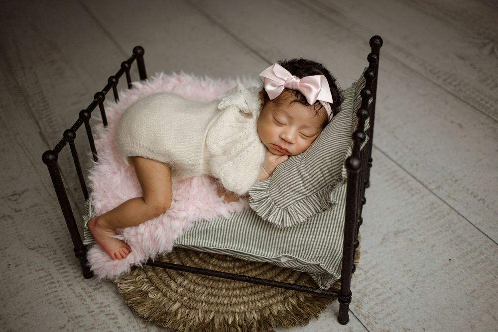 Newborn sleeping peacefully on antique metal bed with ruffled pillows and pink tulle accessories.