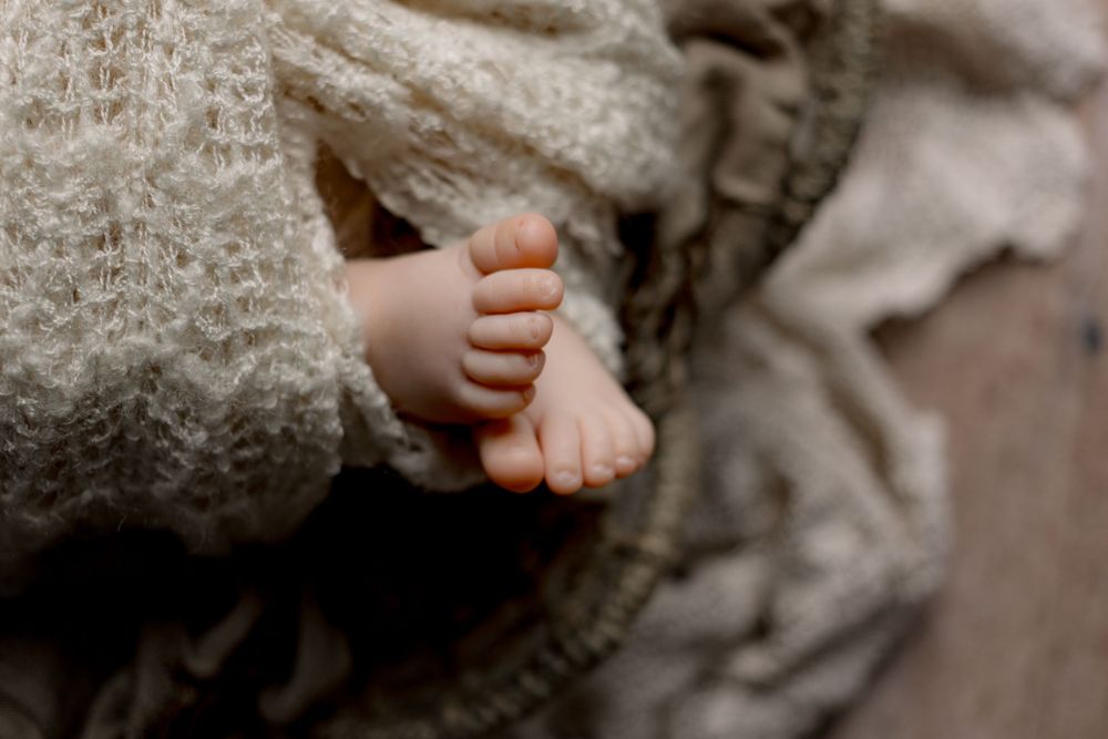 Tiny infant foot wrapped in soft knitted gray blanket shown in close-up detail.