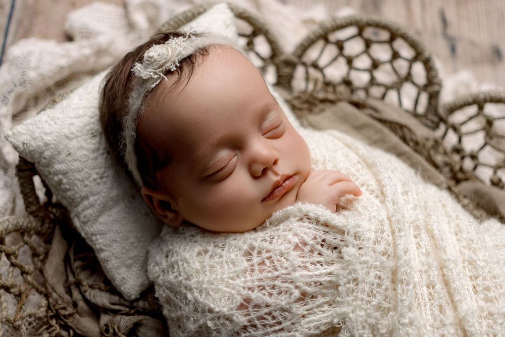 Sleeping newborn wrapped in delicate white lace swaddle resting on vintage textured background.
