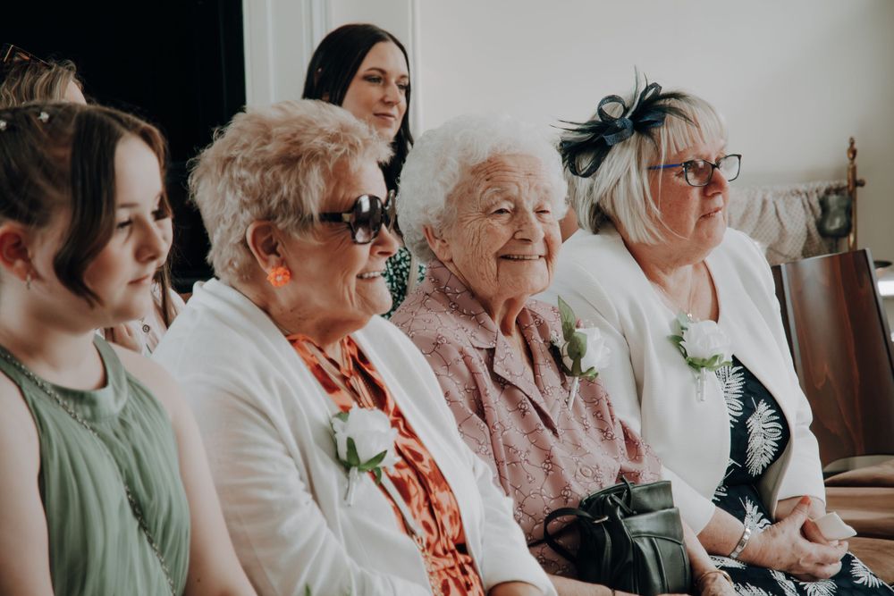 A group of wedding guests sitting together wearing floral boutonnieres and matching formal attire.
