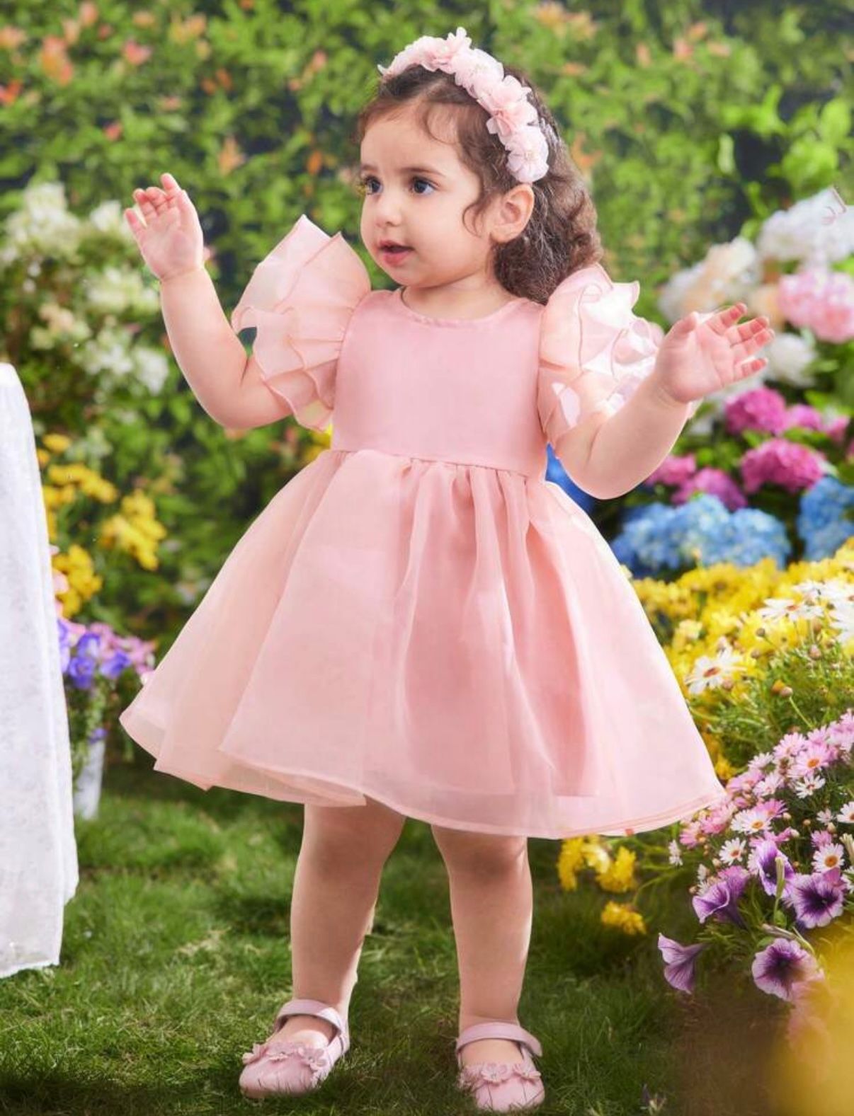 Toddler in a pink tulle dress twirling among colorful garden flowers.