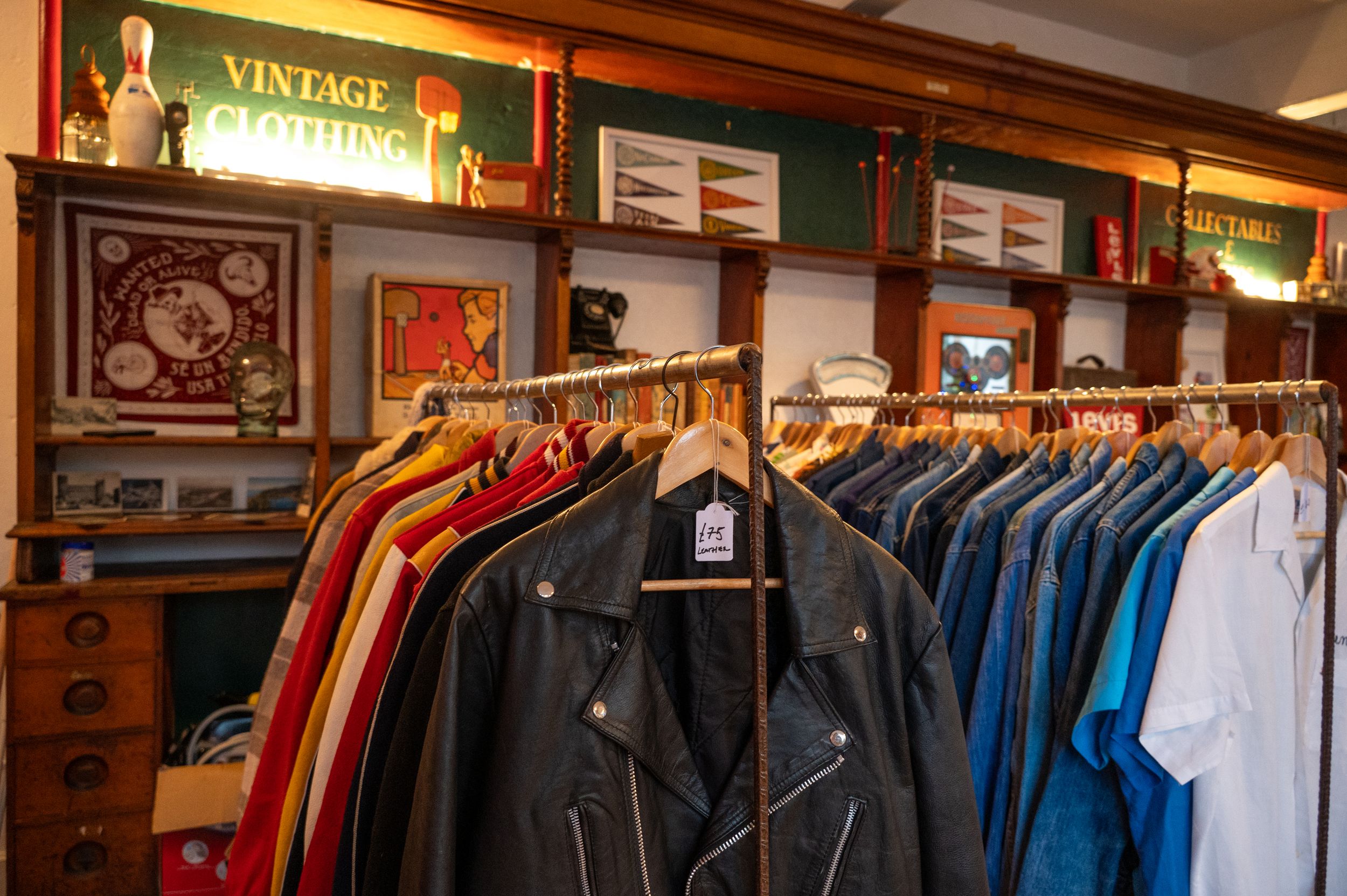 Vintage clothing store interior with racks of colorful jackets and shirts displayed beneath decorative wall art.