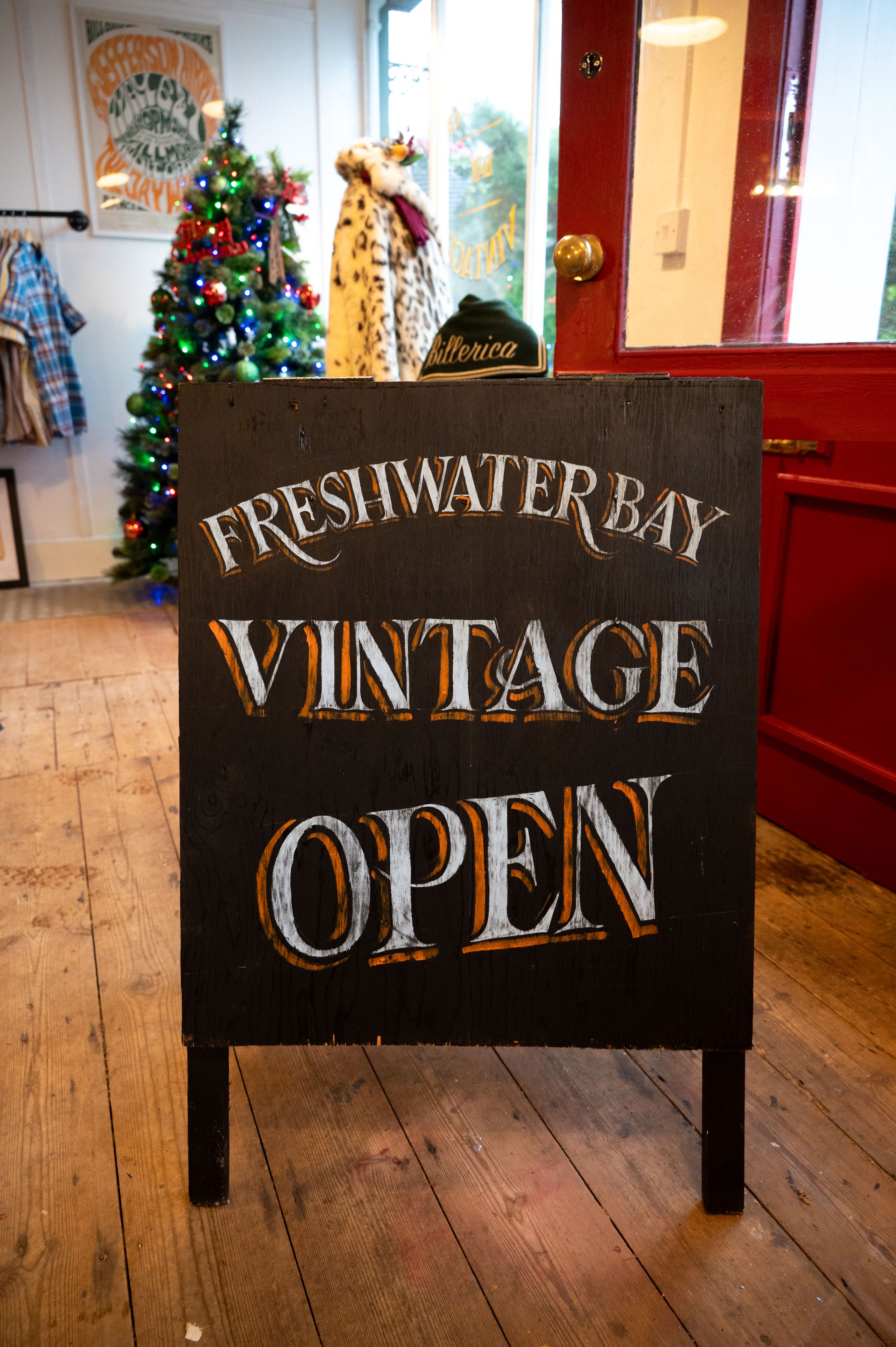 A black chalkboard sign reading 'Freshwater Bay Vintage Open' stands in front of a Christmas tree and wooden floor.