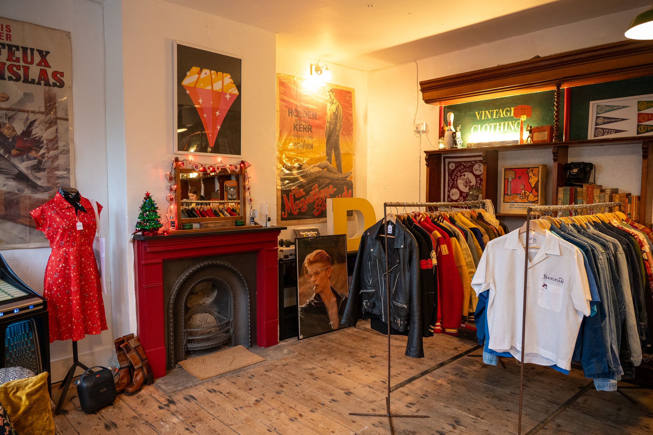 Vintage clothing store interior with red fireplace, hanging garments, and retro posters in warm lighting.