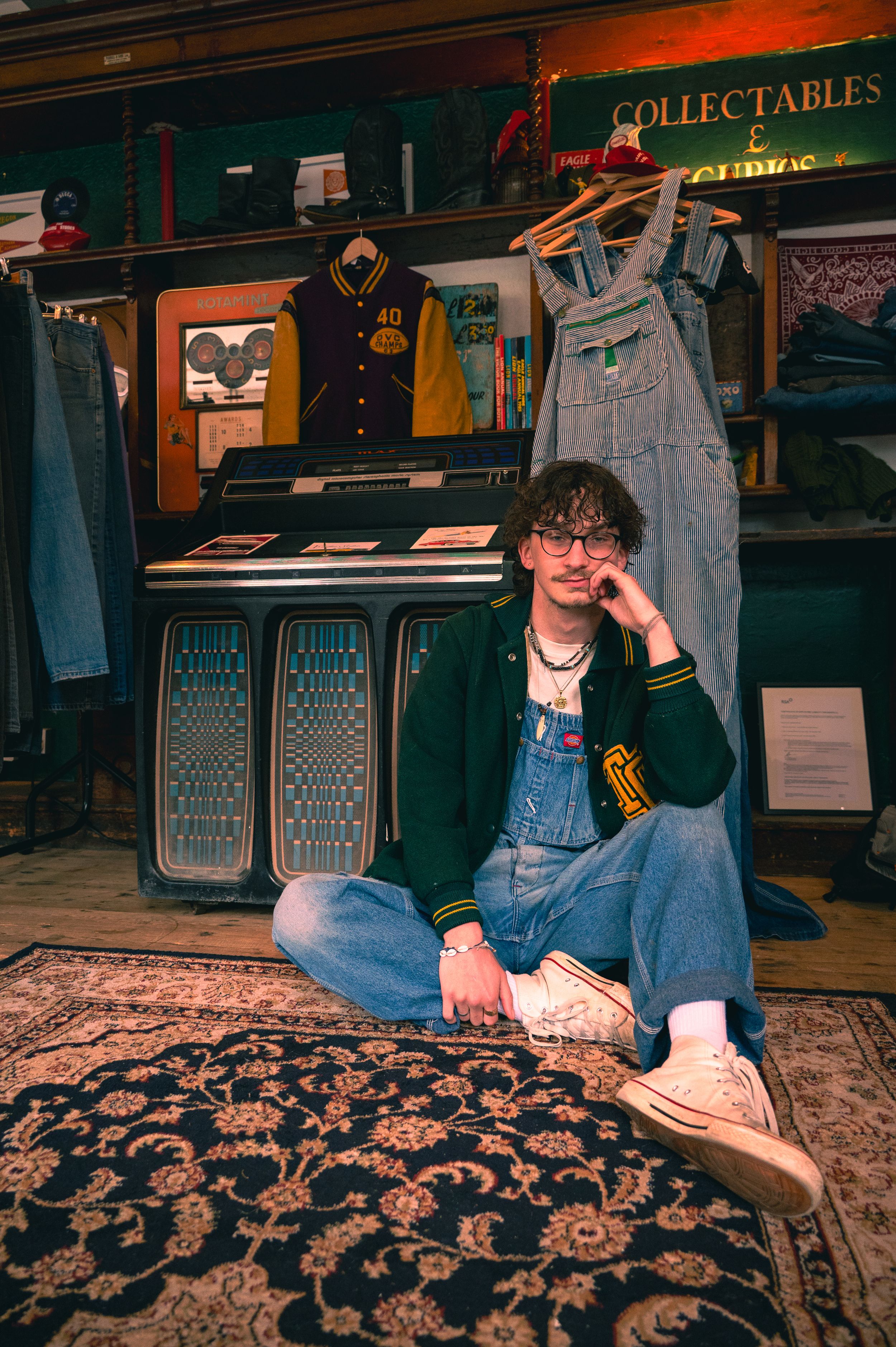 A vintage clothing store interior with collectibles sign, varsity jacket, overalls and decorative patterned carpet on display.