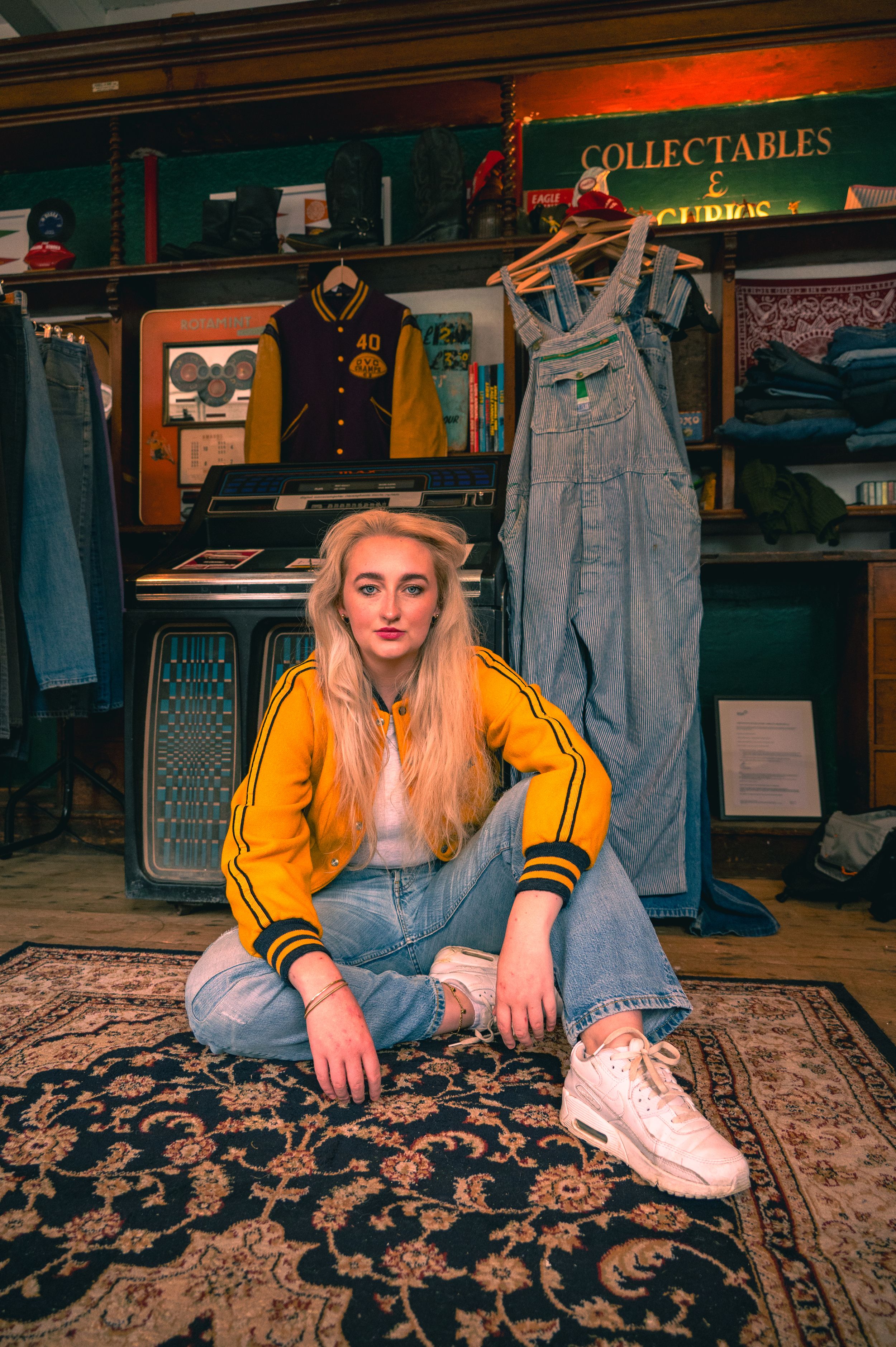 A vintage clothing store interior with overalls displayed and a floral rug on the floor in warm ambient lighting.