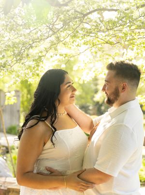 A loving couple shares a romantic moment under blooming spring tree branches in soft golden sunlight.