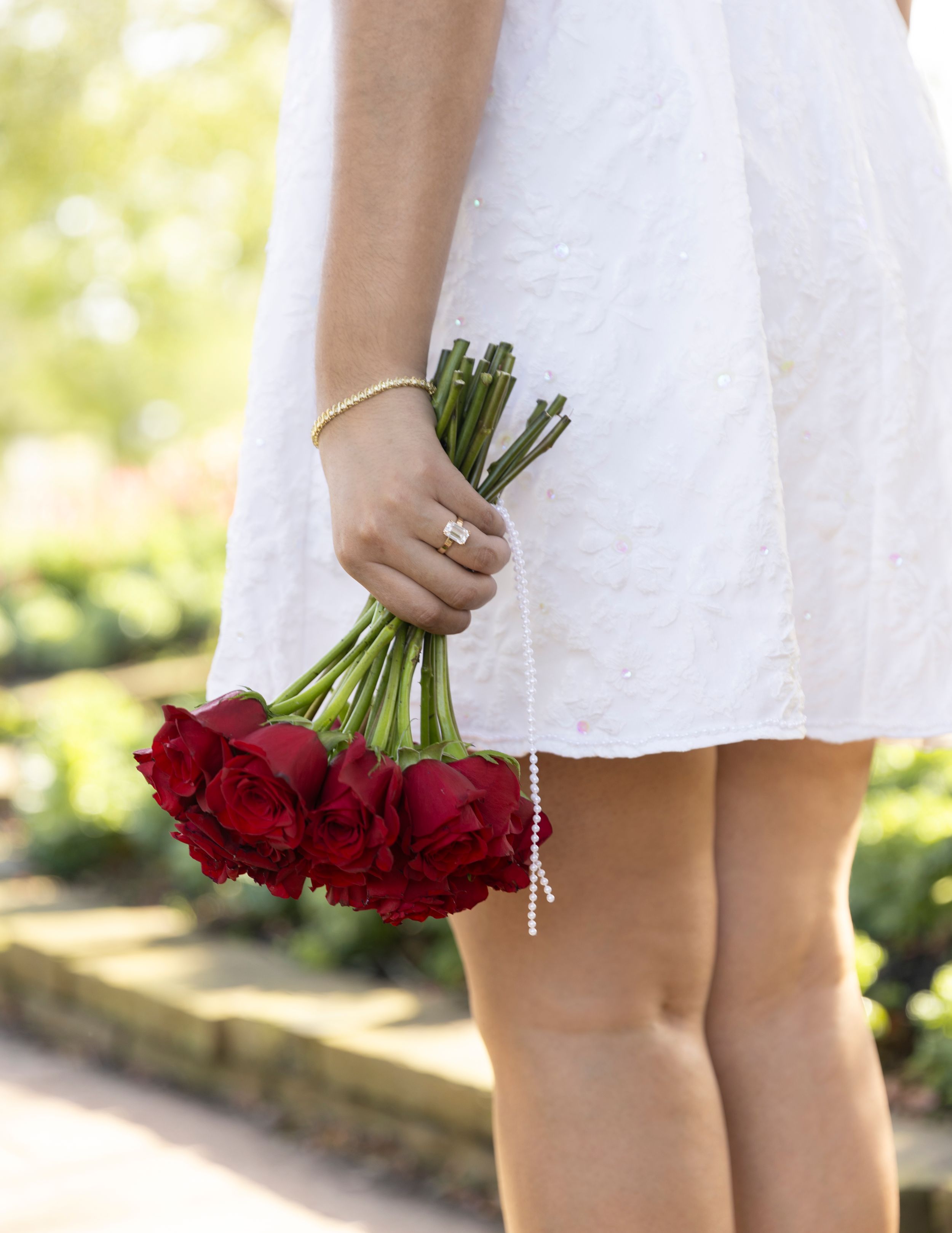 Someone in a white dress holds a bouquet of deep red roses against a soft outdoor background.