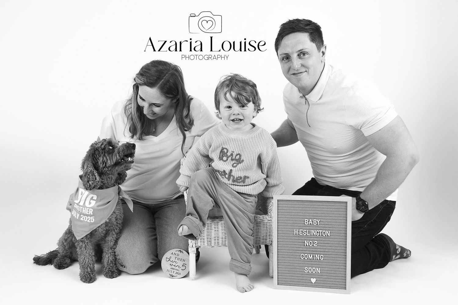 A family poses with their dog alongside a milestone board for a black and white portrait photography session.