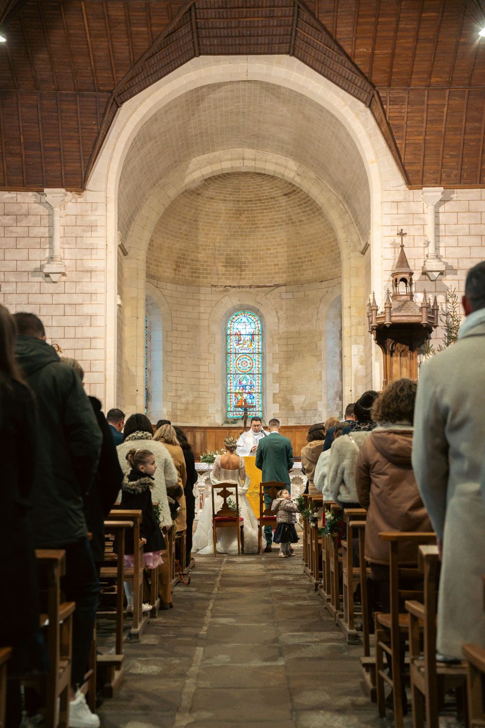 Interior of stone church with stained glass window during wedding ceremony service.