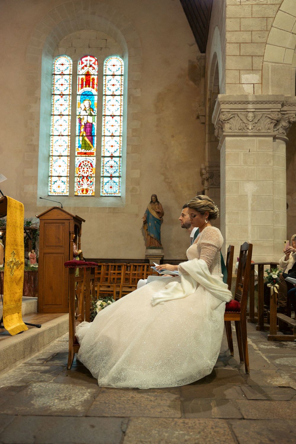 Elegant white wedding gown displayed in a historic church interior with stained glass windows and stone architecture.
