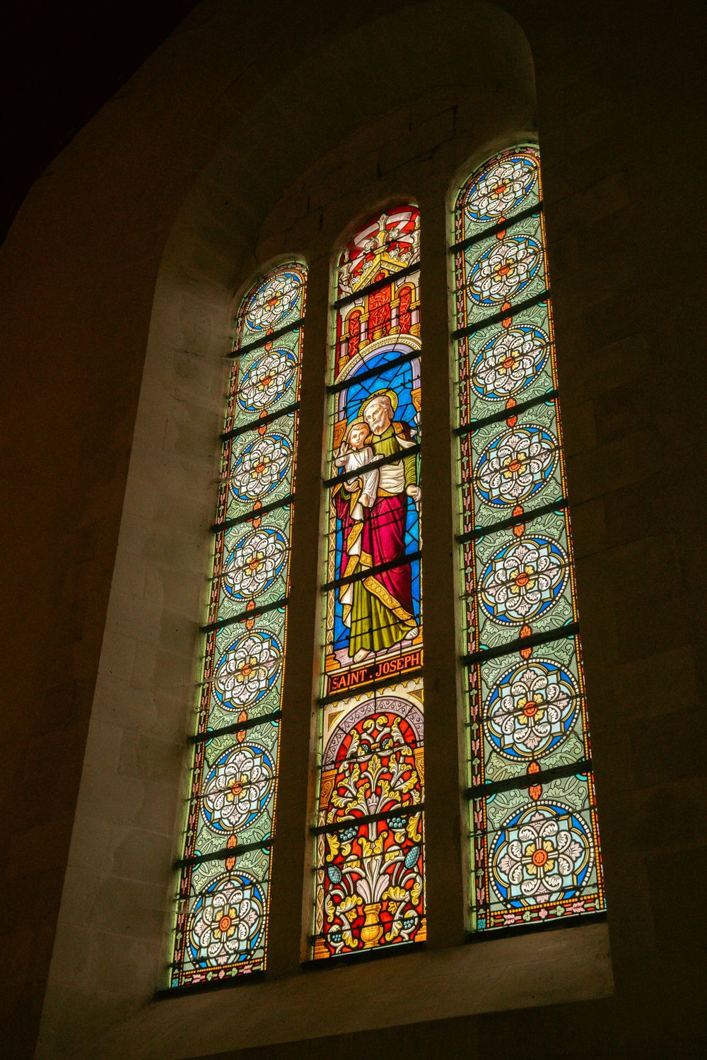 Ornate stained glass church window featuring religious figures with vibrant blue and red colors.