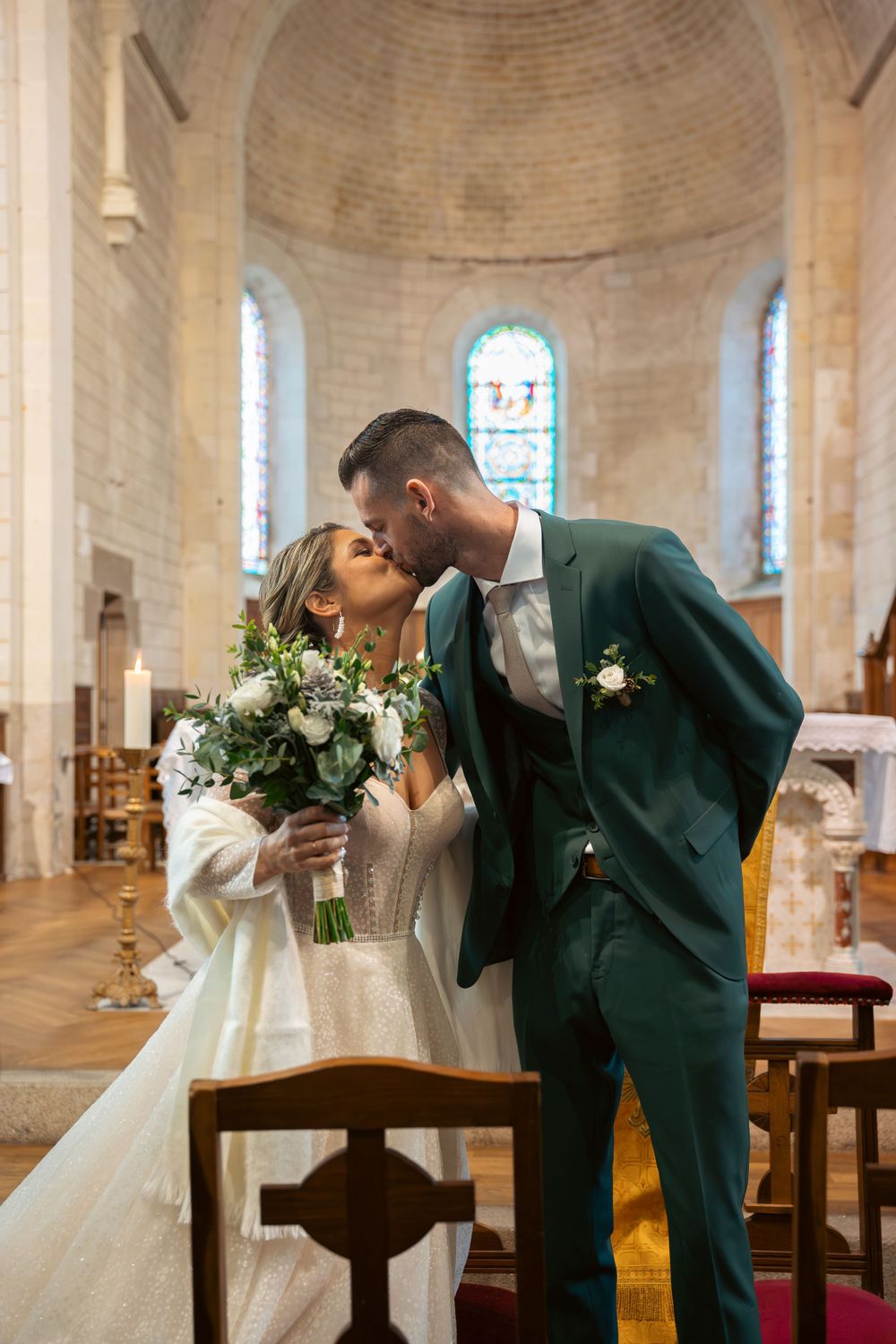 Romantic wedding moment inside a historic stone church with stained glass windows in the background.