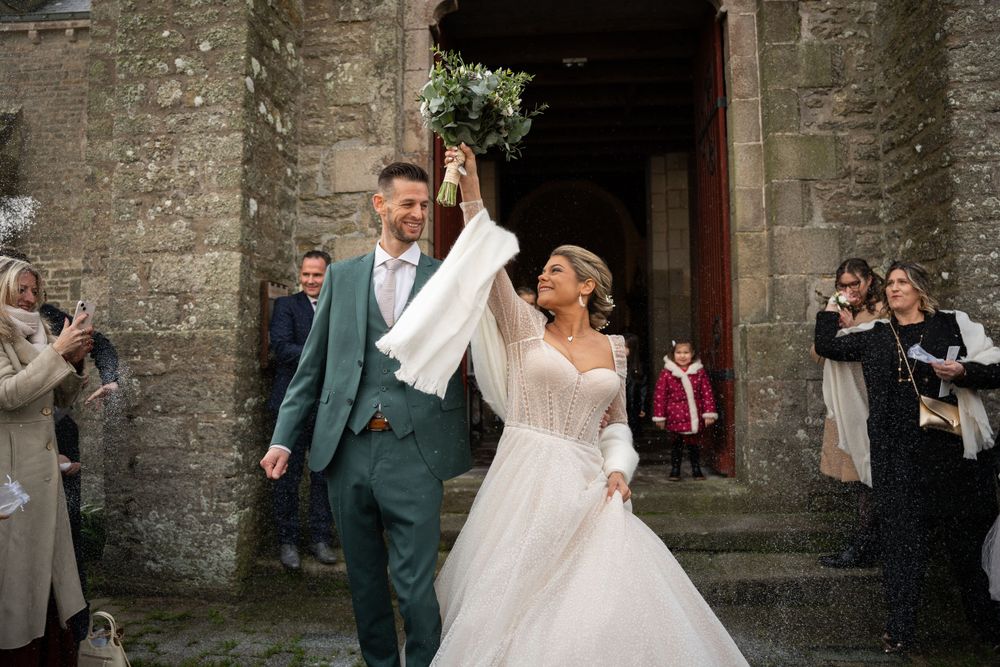 Joyful wedding couple exiting church while guests applaud and celebrate.