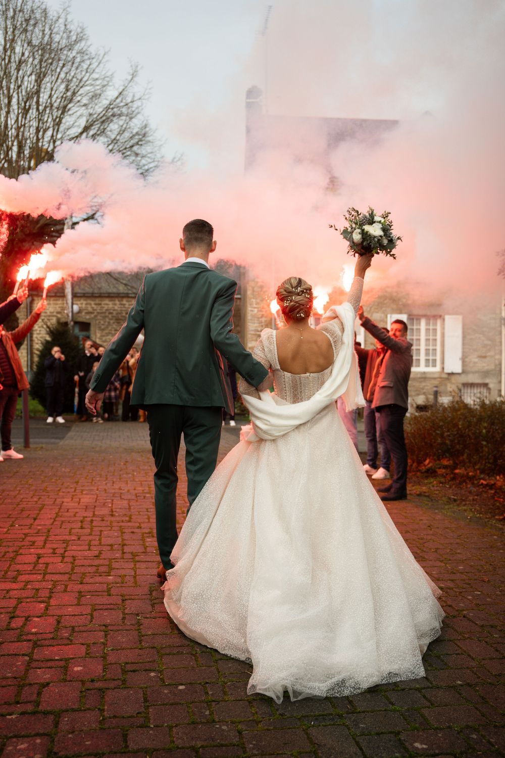 Newlyweds walking through a spectacular red smoke celebration display on brick pathways during their outdoor wedding reception.