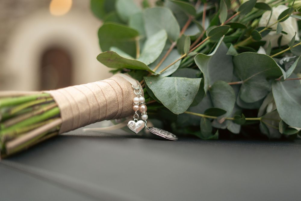A wedding bouquet with eucalyptus leaves wrapped in twine with an engagement ring elegantly placed on top.