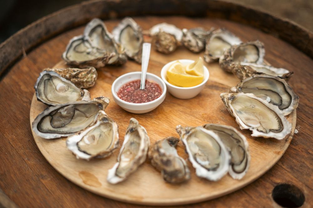 Fresh oysters arranged in a circle on wooden platter with dipping sauces in the center.