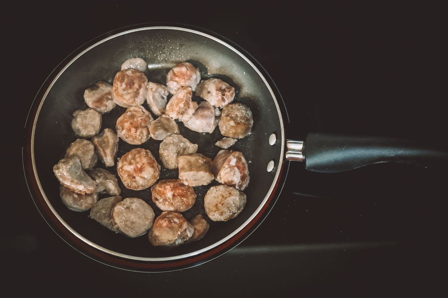 Fresh brown mushrooms cooking in a black nonstick pan against dark background.