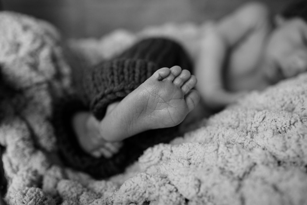 Close-up black and white photo of a tiny baby foot peeking out from under a knitted blanket.