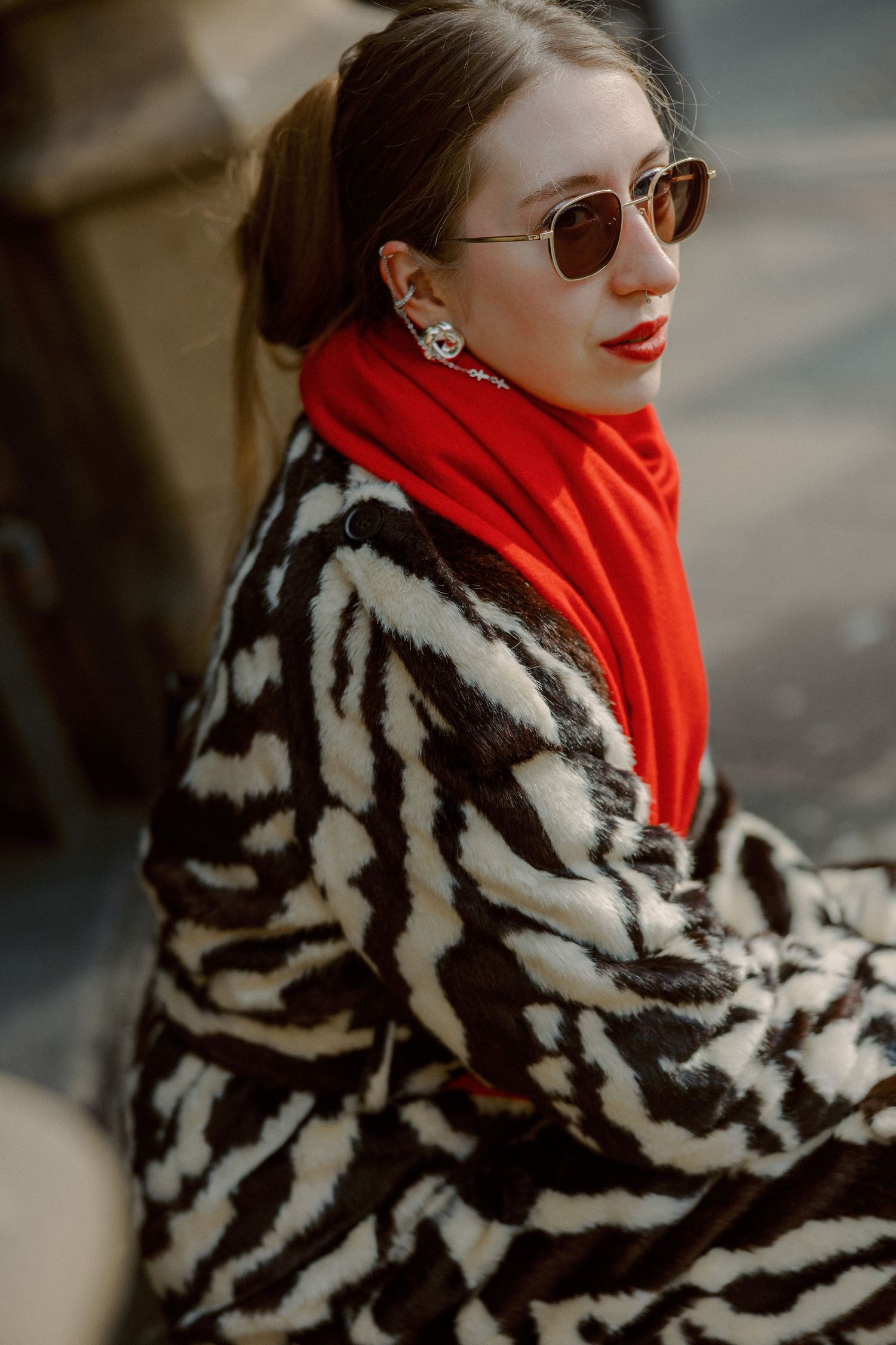 Stylish winter fashion with striped faux fur coat and red scarf against a backdrop of orange autumn flowers.