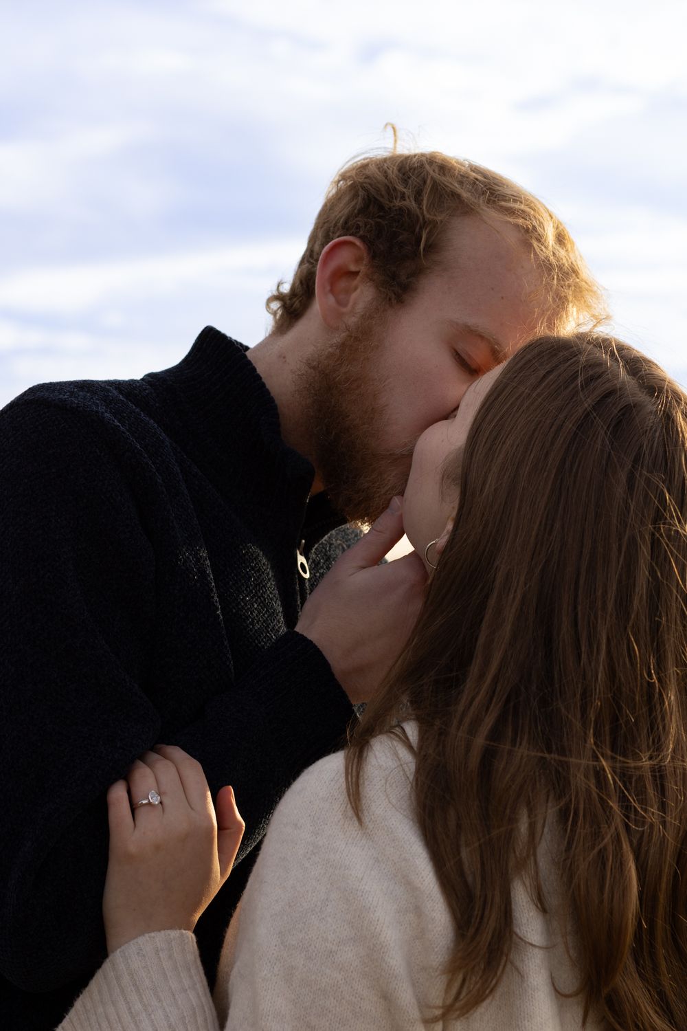 Romantic embrace against cloudy sky during engagement photoshoot.