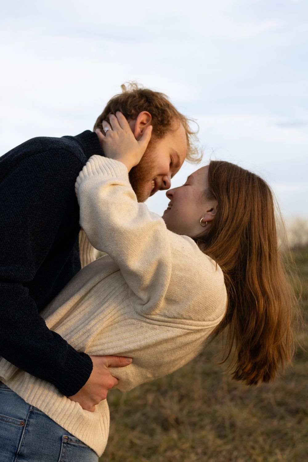 Tender moment captured between couple in cream sweater and black jacket outdoors.