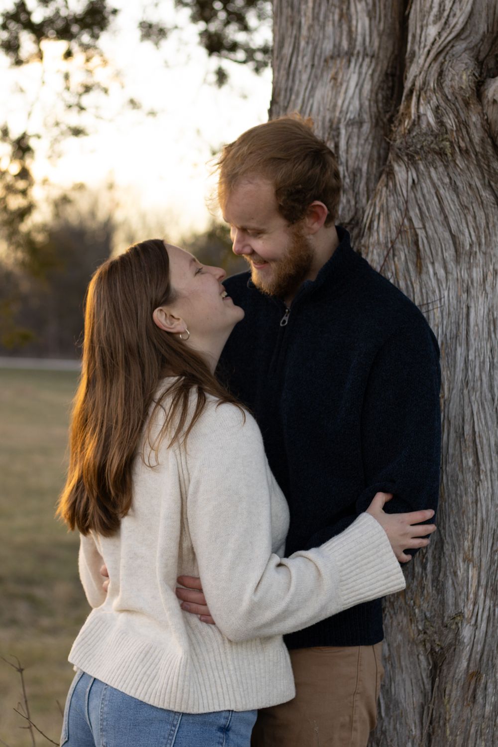 Sweet engagement photos taken against large tree trunk in natural lighting.