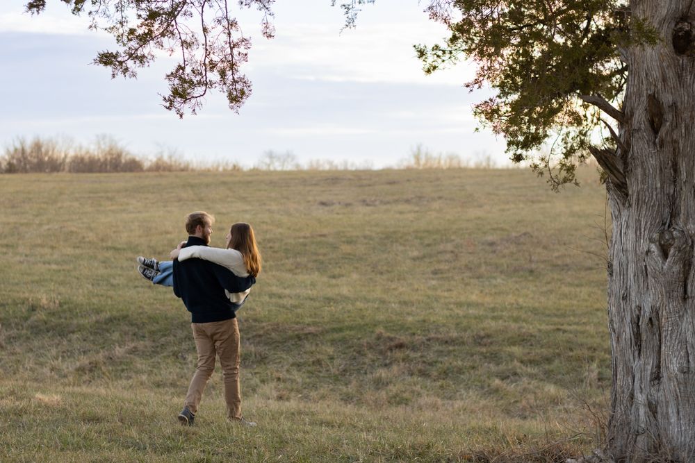 A couple embracing in a golden field during sunset with autumn trees in the background.