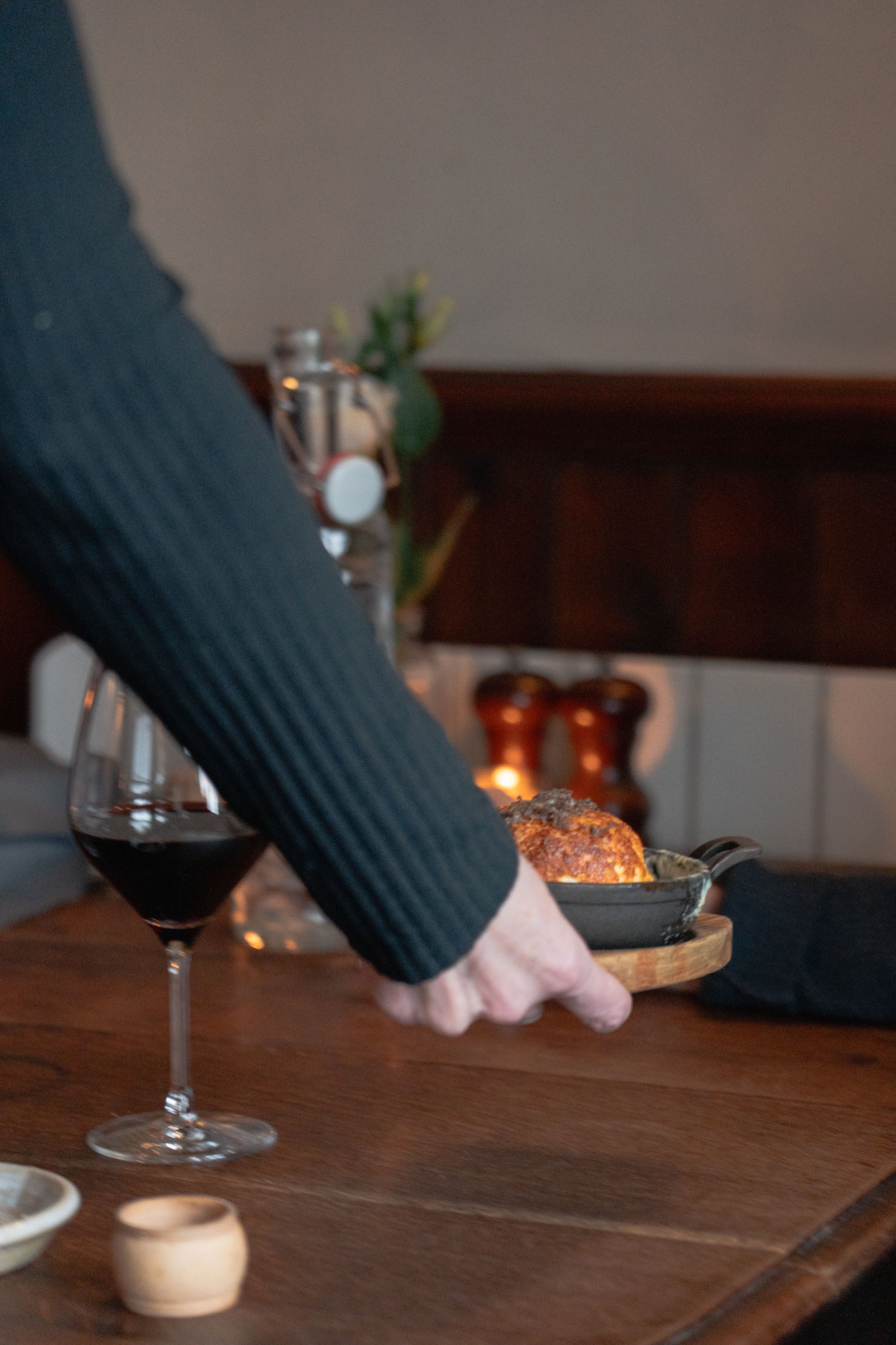 Hand reaching for a plate on a wooden table with a glass of red wine and candlelight creating a cozy dining atmosphere.