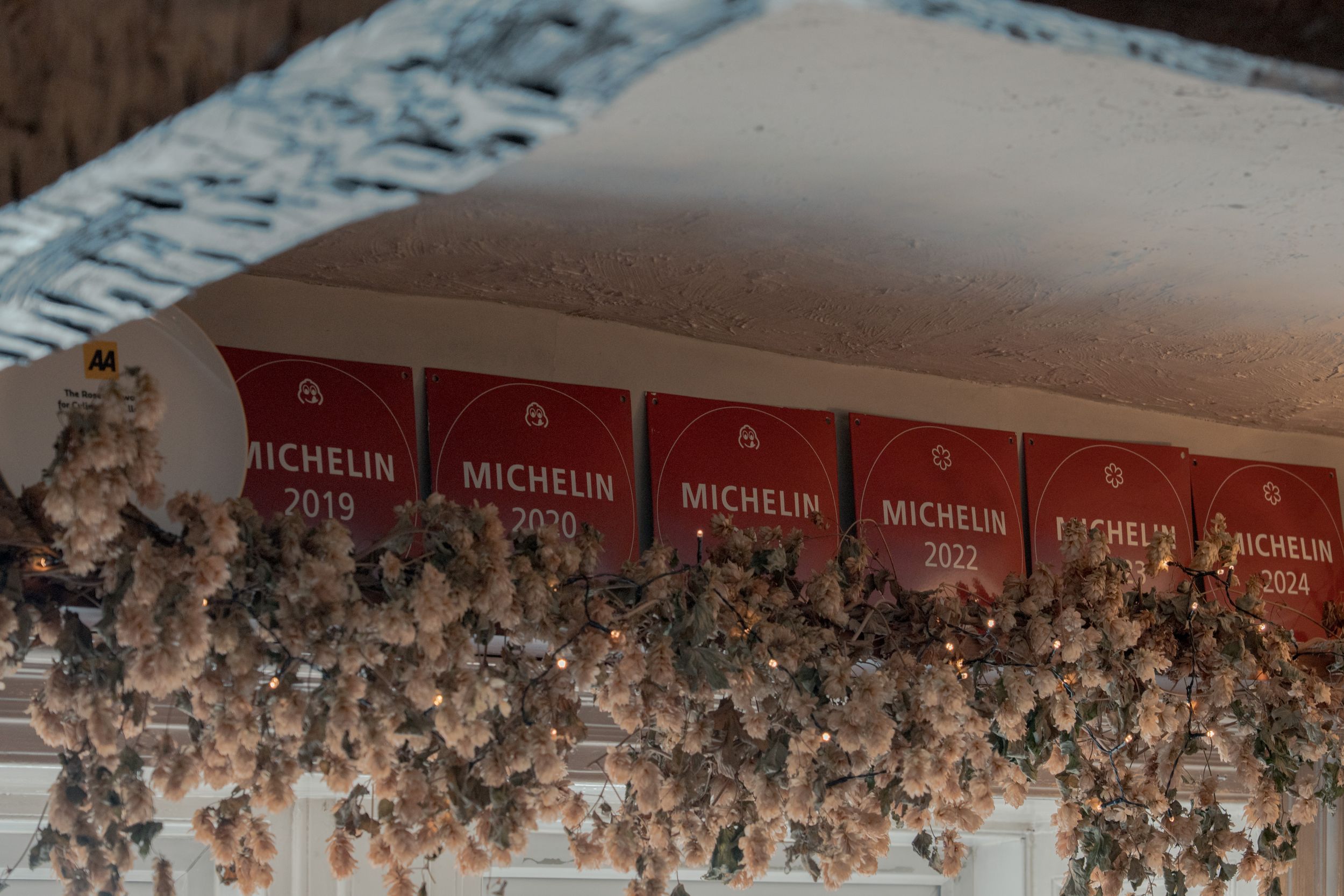 Dried flowers and Michelin guide signs decorate the ceiling of a cozy restaurant.