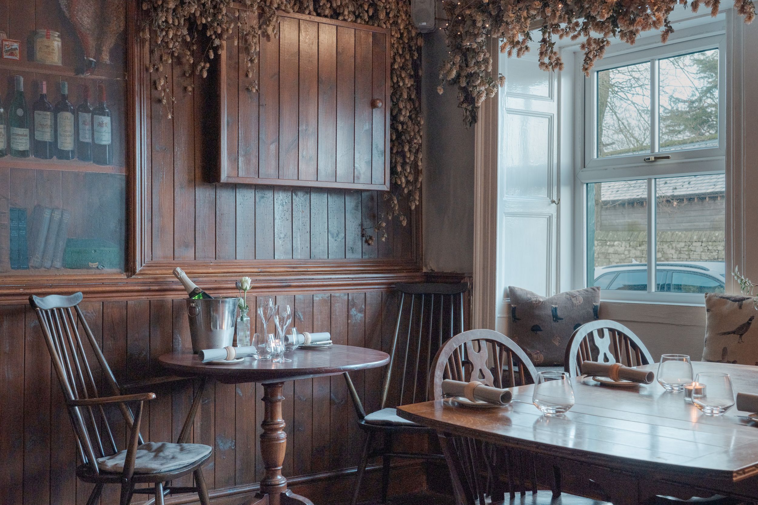 Rustic dining room with wooden chairs and dried flowers hanging from ceiling beams.