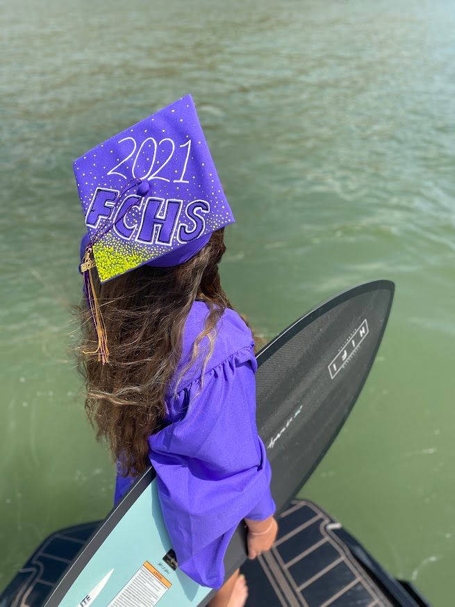 girl standing on boat in water holding a surf board looking out towards the water