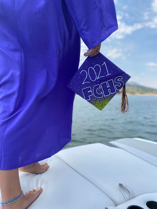 person standing on back of boat holding a graduation cap