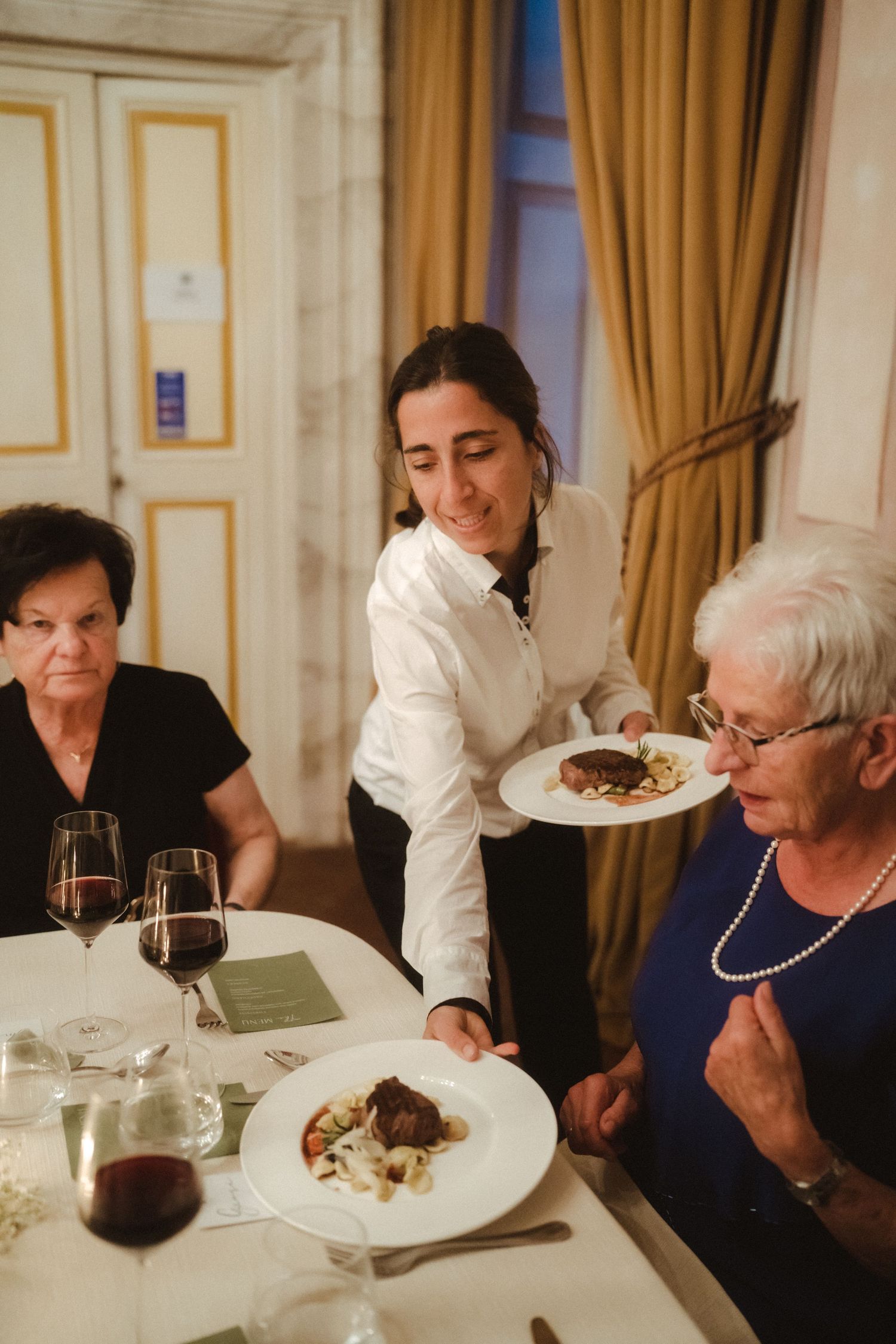 Guests dining at an elegant table with gold-trimmed walls and curtains.