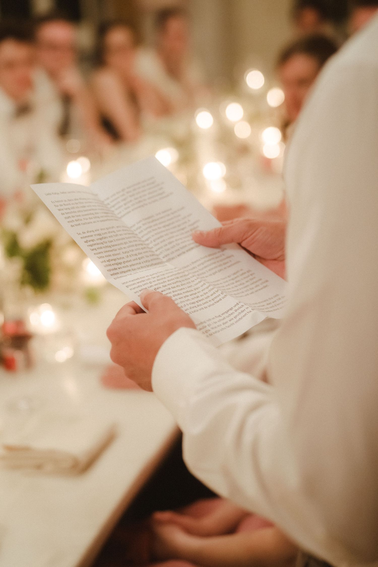 People in formal attire reading from papers at a candlelit dinner table.