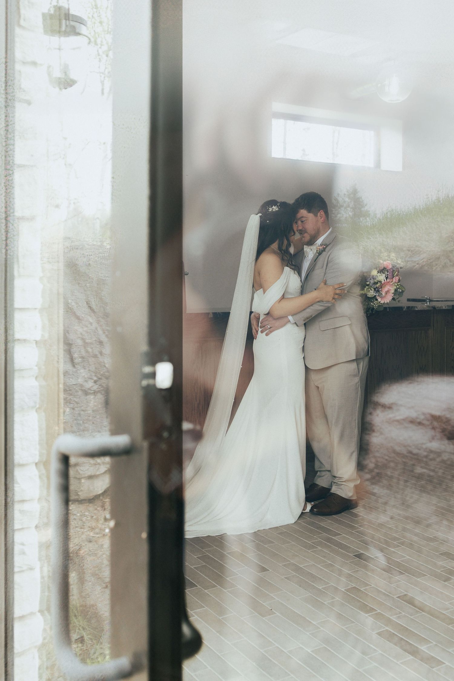 bride and groom embrace during intimate moment, experience focused wedding candid moment caught from outside looking in at couple in Moncton