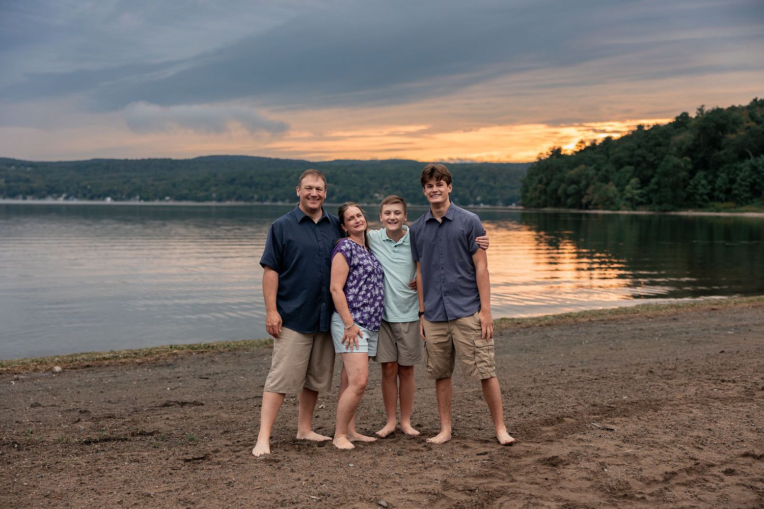 Group of people enjoying a scenic sunset on a sandy beach near mountains and water.