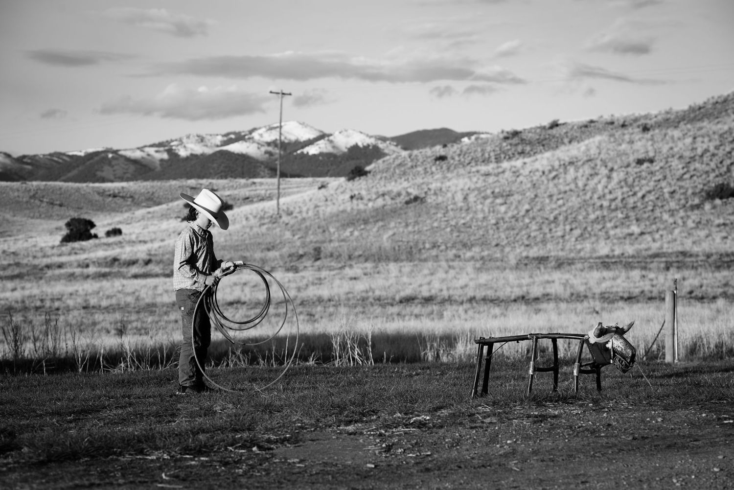 A panoramic black and white landscape photo shows rolling hills with scattered trees and fencing in rural countryside.