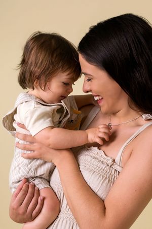 Joyful interaction between parent and baby showing loving connection against beige backdrop.