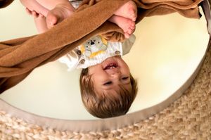 A playful moment captured in a circular mirror reflection showing a child laying down and smiling.