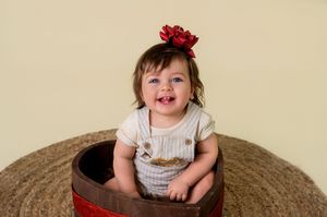 A child in a white shirt sits on a brown circular rug with a red bow in their hair.