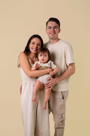 A family portrait showing three people in light colored clothing against a beige studio backdrop.